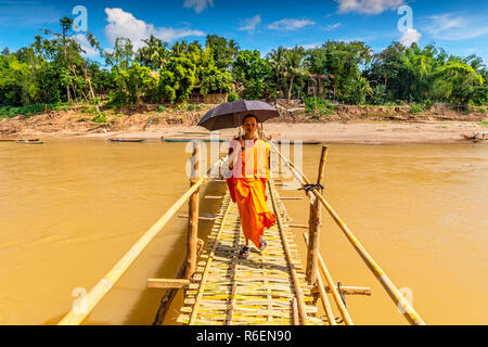 A Young Buddhist Monk Walks Across A Bamboo Bridge Over Nam Khan In Luang Prabang Laos Stock Photo