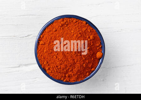 Chili paprika powder in cast iron bowl on white wooden background, view directly from above. Stock Photo