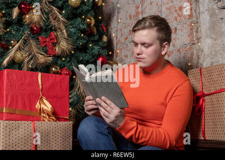 Handsome guy is reading a book sitting under the tree surrounded by gifts Stock Photo