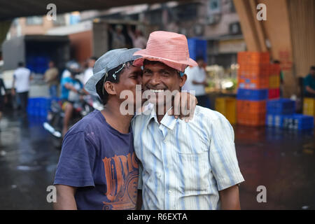 Two cheerful porters at a fish market behind Crawford Market in Mumbai, India, one planting a playful kiss on his friend Stock Photo