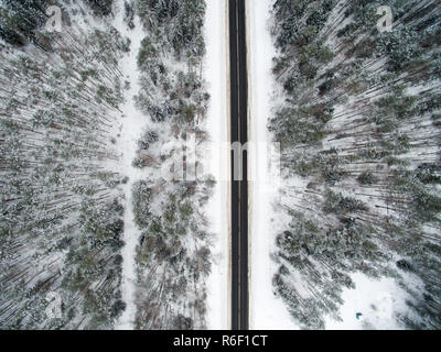 Winter forest and asphalt road. View from above. The photo was taken with a drone. Pine and spruce forest with a black road in the snow. Stock Photo