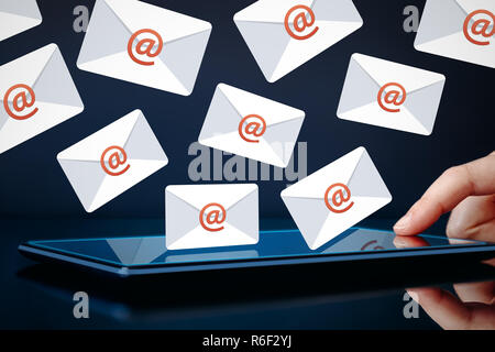 Newsletter and email marketing concept. Hand touching tablet showing email icons on dark background. Stock Photo