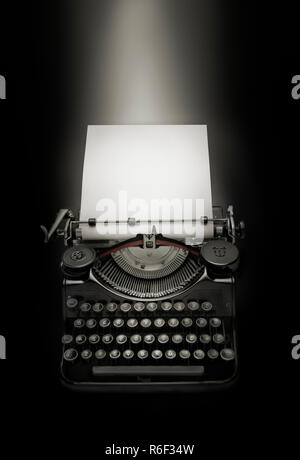 Ancient typewriter and white page against black background Stock Photo