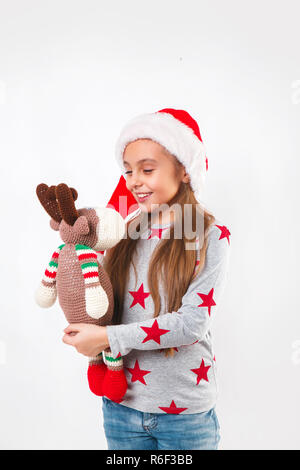 Cute little child in Santa hat with knitted toy deer . The girl laughing and enjoying the gift. Christmas concept Stock Photo
