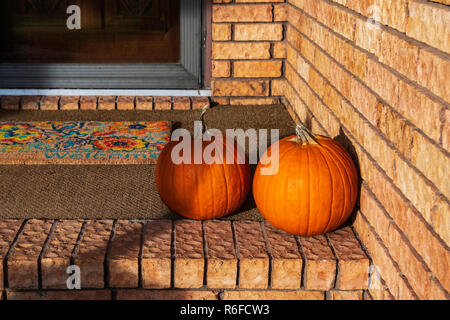 Two mid-sized pumpkins, Cucurbita pepo or winter squash, sitting on the porch of a brick home, used for decor in autumn. Wichita, Kansas, USA. Stock Photo