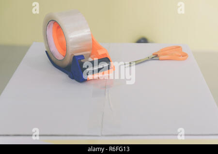 https://l450v.alamy.com/450v/r6fg13/close-up-of-parcel-box-with-scissors-and-scotch-tape-cutter-preparing-a-parcel-or-package-for-shipping-and-delivery-delivery-concept-and-shipping-r6fg13.jpg