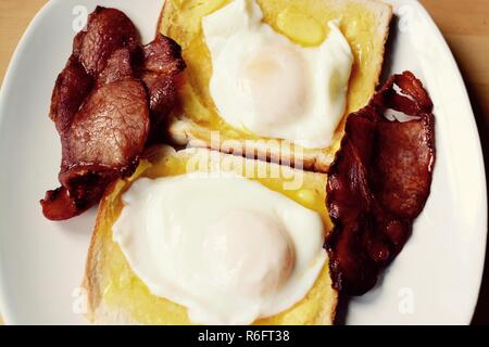 Poached eggs on white buttered toast with crispy bacon, filter applied Stock Photo