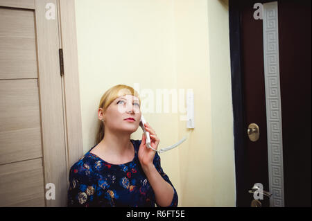 blonde woman answers the intercom call, hold the phone to his ear, waiting for the arrival of the long-awaited guest. Being in apartment near front door Stock Photo