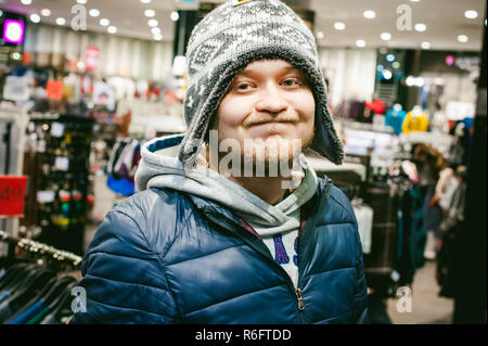 Portrait of a man with a beard with a mustache, putting on winter spring knitted hats in the store, with an emotional face shopping Stock Photo