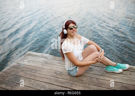 Image of woman in headphones sitting on wooden bridge Stock Photo