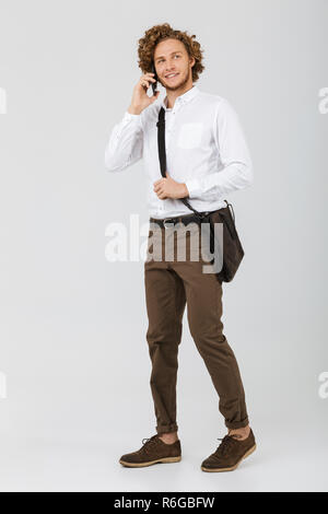 Full length portrait of a smiling businessman dressed in shirt isolated over white background, talking on mobile phone Stock Photo