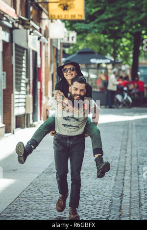 Young man carrying his girlfriend on his back in an urban environment Stock Photo