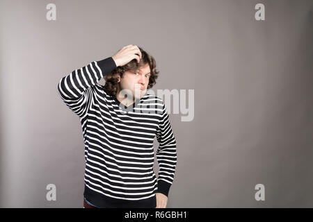 Puzzled guy with messy hair, frowning and looking unsatisfied scratching head, thinking deeply about something on grey wall background. Human facial expression, emotion, feeling, sign body language Stock Photo
