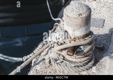 Mooring bollard with tied naval ropes stands on concrete pier in harbor, close-up photo Stock Photo