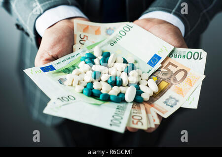 closeup of a young caucasian businessman, wearing an elegant gray suit, with a pile of euro bills and pills of different colors in his hands Stock Photo