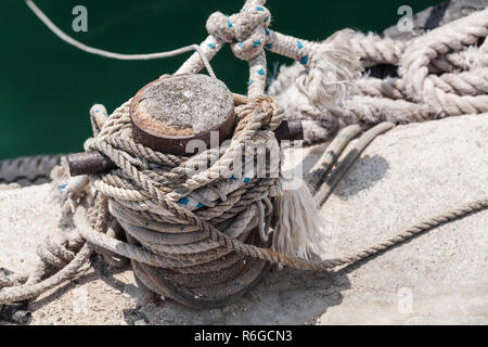 Old rusted mooring bollard with naval ropes stands on concrete pier in harbor Stock Photo