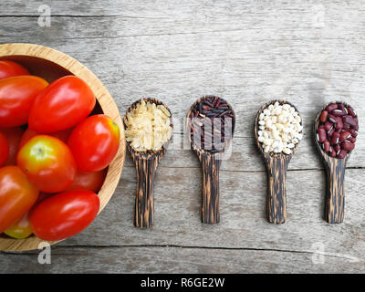 seed on wood spoon and tomato bowl /grains or cereals seeds on wooden spoon various kinds of grains with red kidney bean , Job's tears , riceberry and Stock Photo