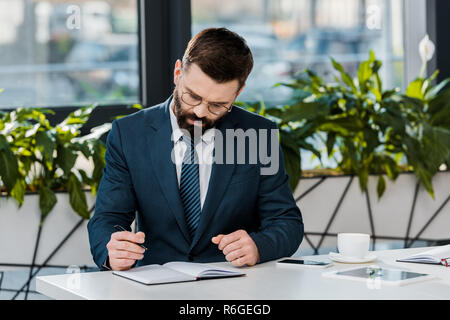 focused bearded businessman writing in notebook at workplace Stock Photo