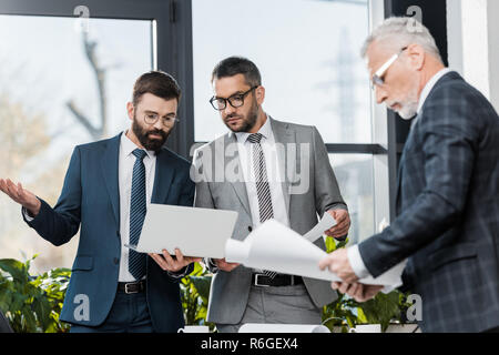 three serious professional businessmen working with papers and laptop in office Stock Photo