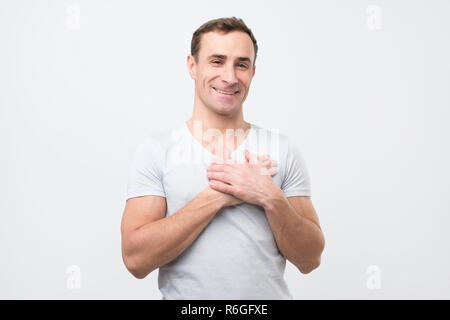 Cheerful man smiles happily, keeps hands on chest, expresses his positive emotions Stock Photo