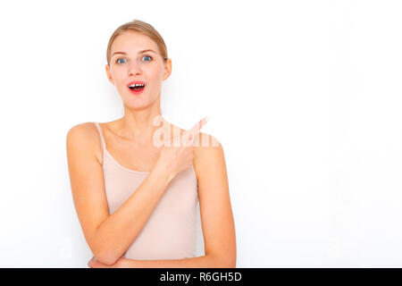 Portrait of happy surprised young woman model indicates with fore finger shows place for your advertisement or promotional text. Stock Photo