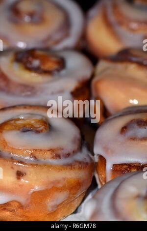 Two rows of sweet cinnamon pastries covered with icing seen from a vertical view. Stock Photo
