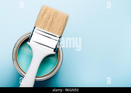 Brush with white handle on open can of turquoise paint on blue pastel background. Renovation concept. Place for text. Stock Photo