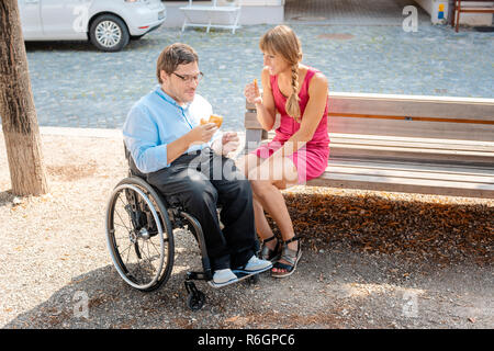 Man in wheelchair and woman eating nibbles spending time Stock Photo