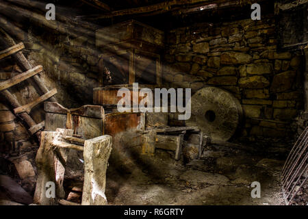 Beautiful sun rays that pass through the cracks on the roof, and illuminate interiors of old water mill, large circular stone, ladders and other satff Stock Photo
