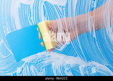 Hand cleaning glass window pane with detergent by sponge. Stock Photo