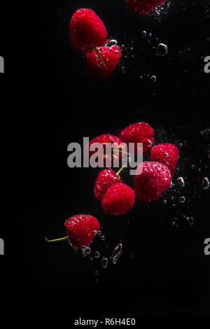 Raspberries falling in water  on a black background. High speed flash splash photography. Fresh raspberries dropped into water.  Copy space. Stock Photo