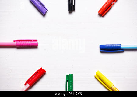Colorful pens on natural white wooden background. Arranged in circle. Copy space in the center. Stock Photo