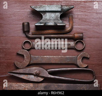 Old rusty rugged anvil and other blacksmith tools on brown natural wooden background in a shape of christmas tree. Flat lay top view. Stock Photo