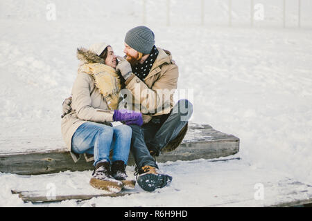 Loving couple young people a man with a beard and a Caucasian woman are sitting on a wooden staircase in the winter on the snow St. Valentine's Day a  Stock Photo