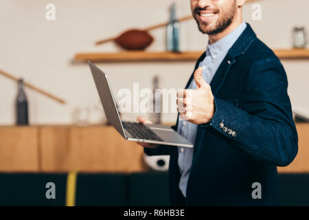 cropped shot of smiling businessman with laptop showing thumb up in cafe Stock Photo