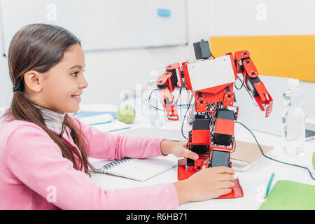 adorable schoolgirl sitting at table in STEM classroom and playing with robot model Stock Photo