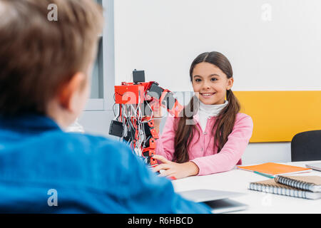 adorable schoolgirl and schoolboy sitting at desk and working together on robot model at STEM class Stock Photo