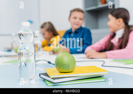 green ripe apple on notebooks and schoolchildren at background in classroom Stock Photo