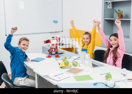 happy children throwing hands in air at STEM robotics lesson Stock Photo