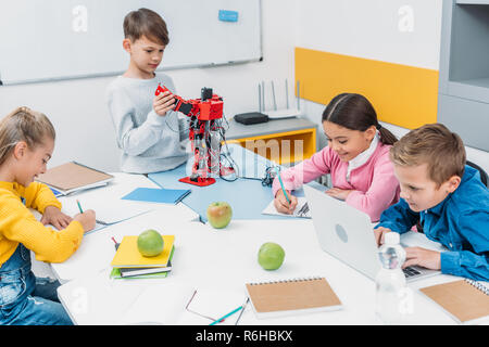 schoolchildren writing, using laptop, working on robot at STEM robotics lesson Stock Photo