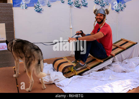 Guy sitting on a sled laughing as he gets his photo taken wearing a viking hat at the Danish festival in Tucson AZ Stock Photo