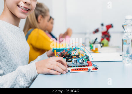 cropped view of schoolboy holding handmade robot model and classmates working together on project during STEM lesson on background Stock Photo