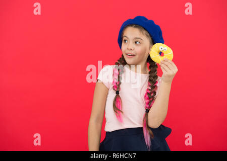 Kid playful girl ready to eat donut. Sweets shop and bakery concept. Kids huge fans of baked donuts. Impossible to resist fresh made donut. Girl hold glazed cute donut in hand red background. Stock Photo