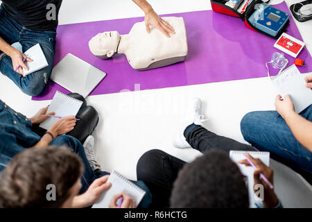 Group of young people sitting in a circle during the first aid courses with medical dummy, close-up view from above Stock Photo