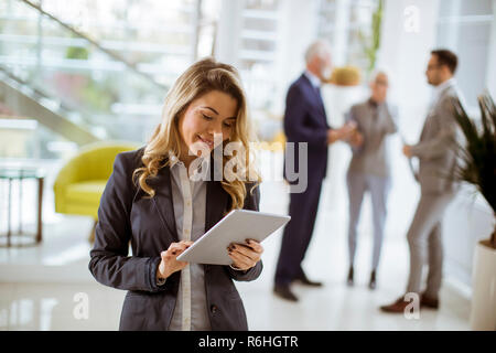 Portrait of young businesswoman using with tablet in office while other business people talking in background Stock Photo