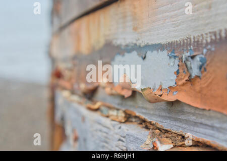 Old orange and white paint peeling off from an old piece of wood that belongs to a boat on a beach. Stock Photo