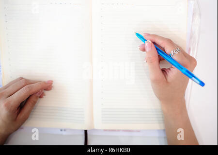 Business woman making notes in notepad. Beautiful well-groomed hands close-up hands, holding a pen, sitting in the workplace Stock Photo