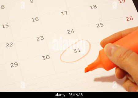 Female hand holds an orange marker pen and circled thirty-first, the last day on the calendar sheet. End of the year and the new year coming concept Stock Photo