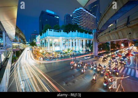Creative high angle night shot of Ratchaprasong Intersection and Erawan Shrine in Bangkok, Thailand, with colourful light trail from cars driving past Stock Photo
