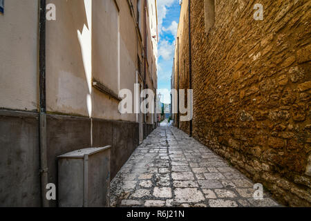 A long and narrow alleyway leading to a blue door is framed by massive, medieval walls in the historic center of Brindisi, Italy Stock Photo